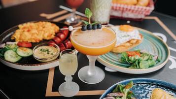 A table with various dishes including a salad, a plate of sausages, a plate of scrambled eggs, and a drink with a garnish.