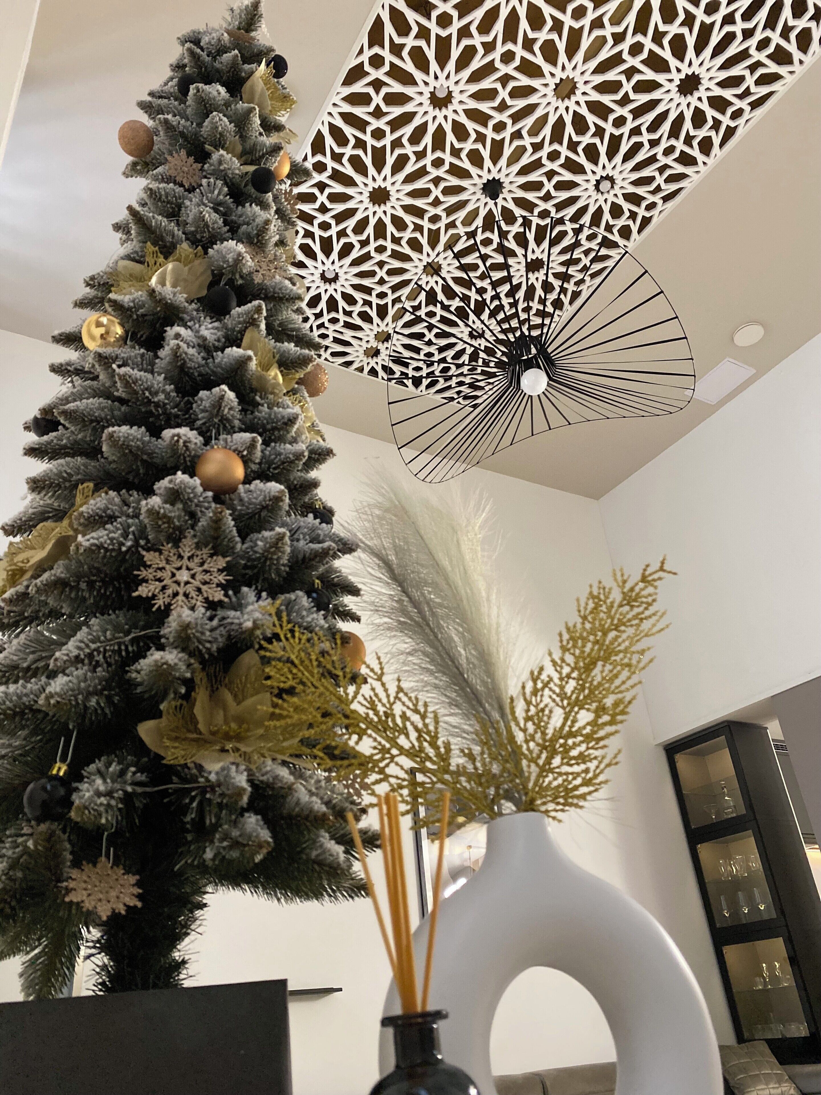 A modern interior with a decorative Christmas tree, a geometric ceiling light, and a minimalist vase with reeds.