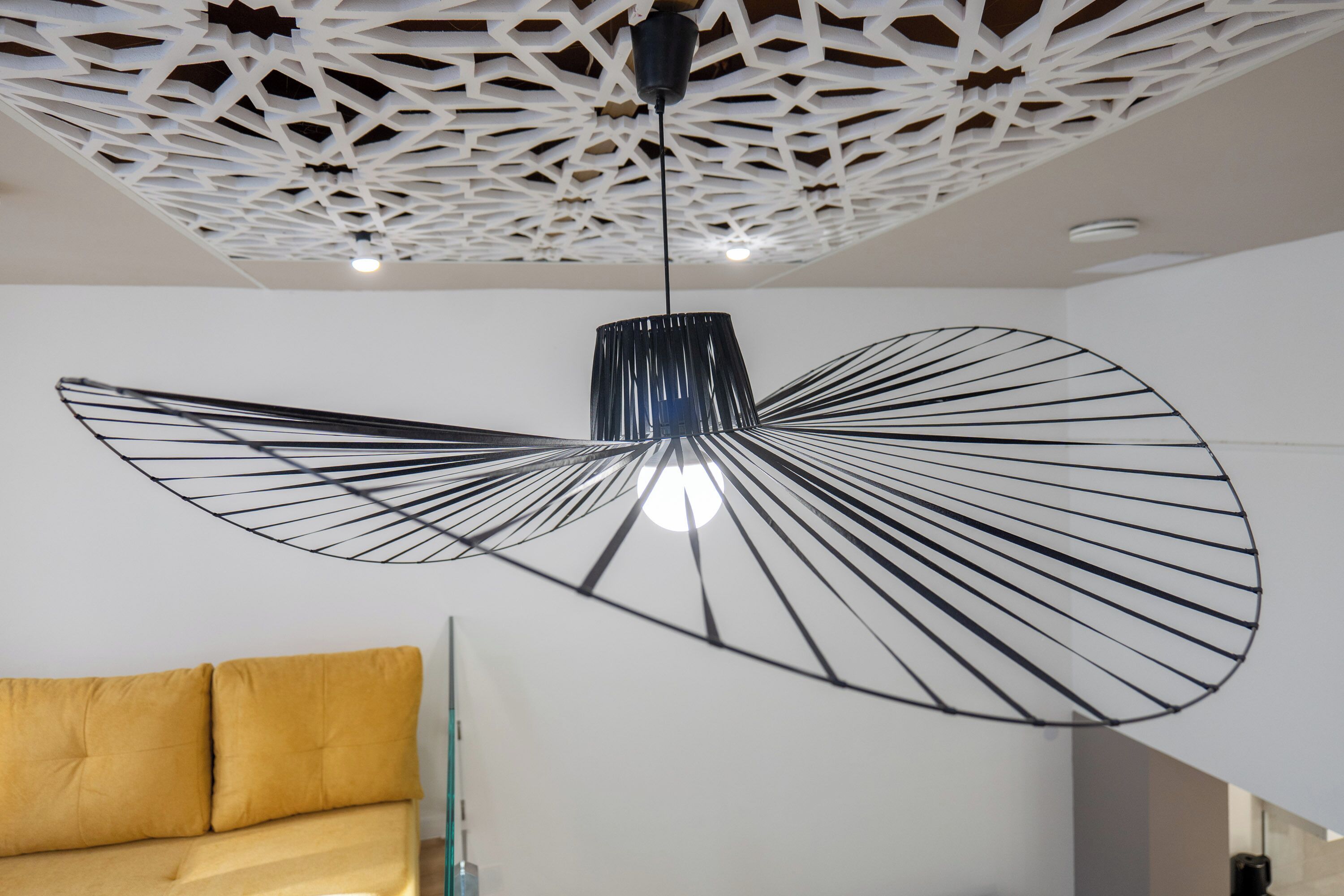 Un intérieur moderne avec un plafond au design original, un luminaire suspendu noir et un canapé jaune.