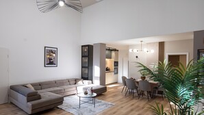 A modern living room with a sectional sofa, a dining area with a table and chairs, and a kitchen in the background. - Z8 Premium Apartman (Kaposvár)