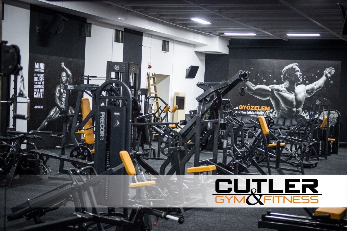Un gimnasio con diversos equipos de ejercicio, carteles motivacionales y una pantalla grande que muestra una figura musculosa.