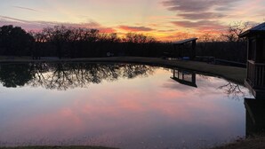 A tranquil lakeside scene at sunset with a wooden dock and a gazebo. - Charming 2-bedroom house on 40 acres in Springtown with pond (Springtown)