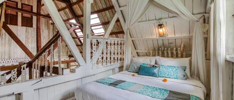 A rustic room with a bed, white curtains, and a hanging light fixture.