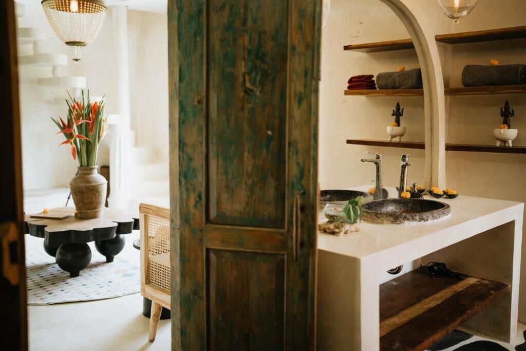 Un baño con un lavamanos blanco, una puerta de madera y estantes con toallas.