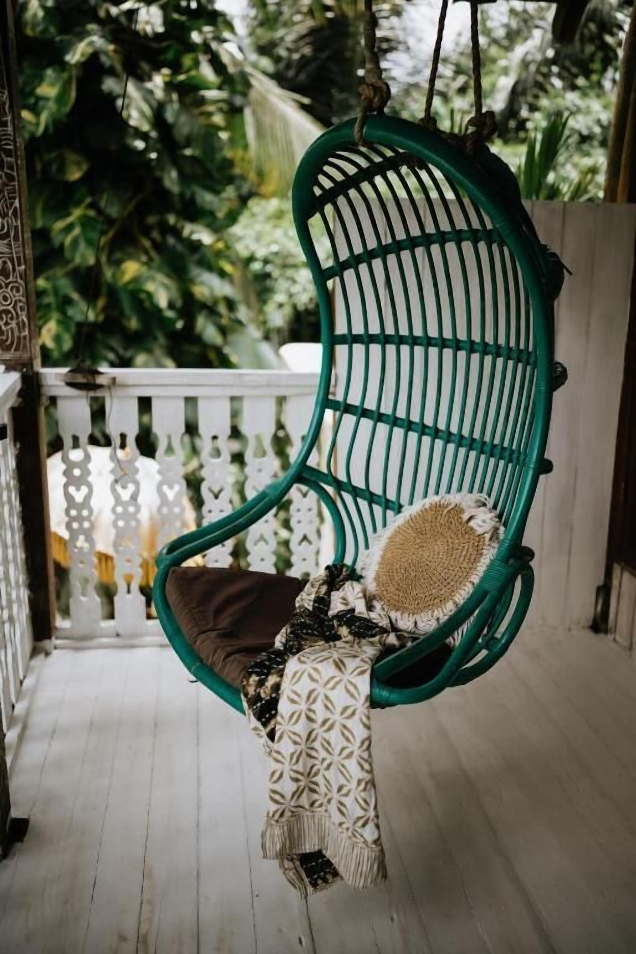 A green hanging chair with a cushion and a patterned throw blanket on a wooden porch.
