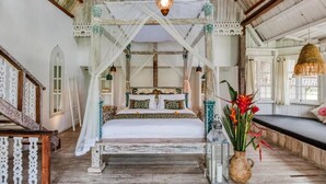 Un lit à baldaquin, un plancher en bois, un mur blanc et un luminaire suspendu.
