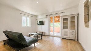 Ein modernes Wohnzimmer mit einem schwarzen Sofa, einem kleinen Tisch, einem Fernseher und einer Glastür, die zu einem Außenbereich führt.