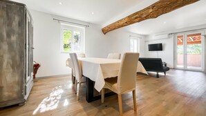 Ein geräumiges Zimmer mit Esstisch, Stühlen, einer Couch und einem Fernseher.