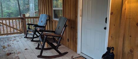 A wooden porch with rocking chairs, a white door, and a bear statue.