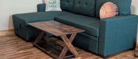 Ein smaragdgrünes Sofa mit einem Holztisch und einem Zierkissen.