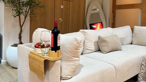 A modern living room with a beige sofa, a wooden sideboard with a wine bottle and glasses, a potted plant, and a sliding wooden door.
