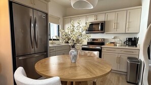 A modern kitchen with a round wooden table, white chairs, a stainless steel refrigerator, and a microwave.