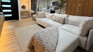 A modern living room with a sectional sofa, a large woven throw blanket, and a dining area in the background.