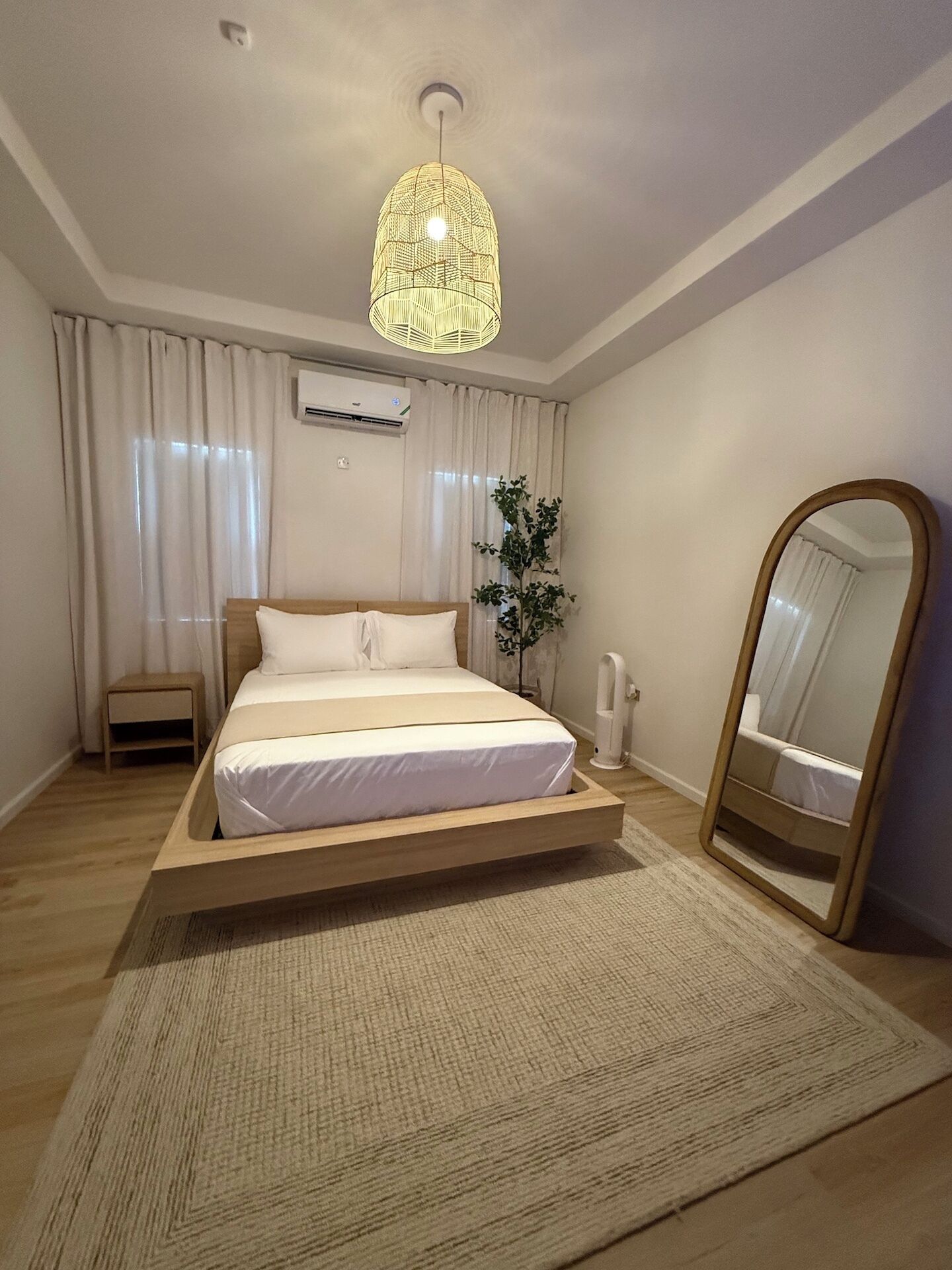 Een moderne slaapkamer met een houten bed, een grote spiegel en een hanglamp.