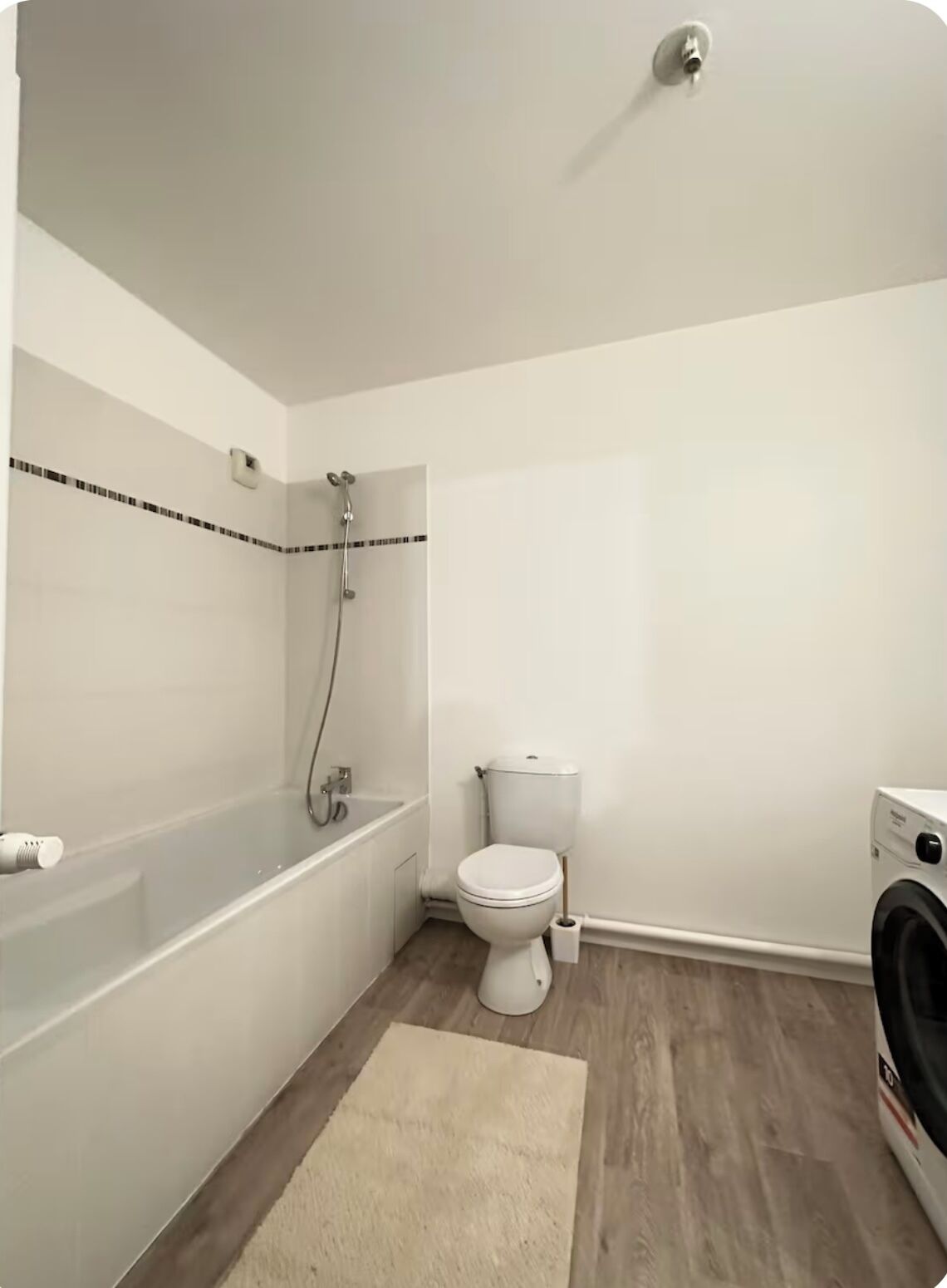 A small, clean bathroom with a white toilet, a bathtub, and a washing machine.