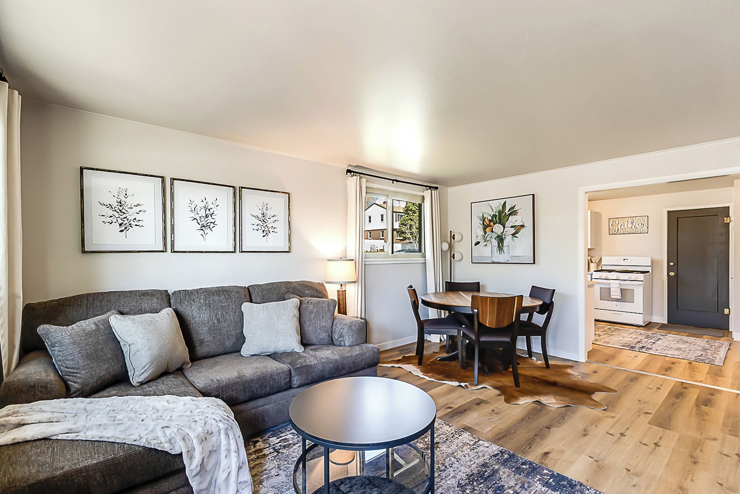 Un salon moderne avec un canapé gris, une table basse ronde et un coin repas comprenant une table et des chaises en bois.