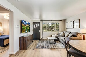 En moderne stue med sofa, spisebord og fjernsyn hængt på væggen.
