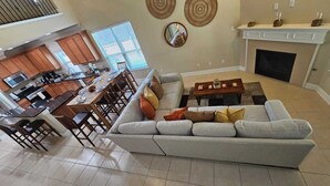Ein modernes Wohnzimmer mit grauem Sofa, Esstisch aus Holz und einer Küche im Hintergrund.