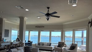 A spacious living room with a view of the water, a ceiling fan, and a 'Weekend Getaway' sign.