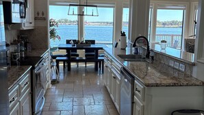 A spacious kitchen with white cabinetry, a granite countertop, and a view of the water.
