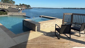 A pool area with a wooden deck, lounge chairs, and a view of the water.