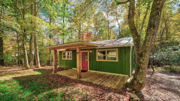 Eine kleine Holzhütte mit Veranda, umgeben von Bäumen und einer Holzterrasse.