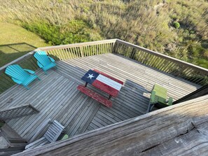 A wooden deck with a Texas flag table, two turquoise Adirondack chairs, and a wooden fence.
