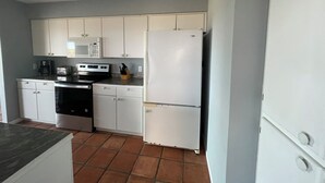 Een keuken met witte kastjes, een magnetron, een fornuis en een koelkast.