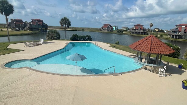 Een zwembad met ligbedden en een parasol, omgeven door water en huizen.