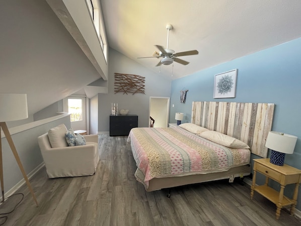 Ein Schlafzimmer mit Bett, Deckenventilator, Kommode, Stuhl und Nachttisch.