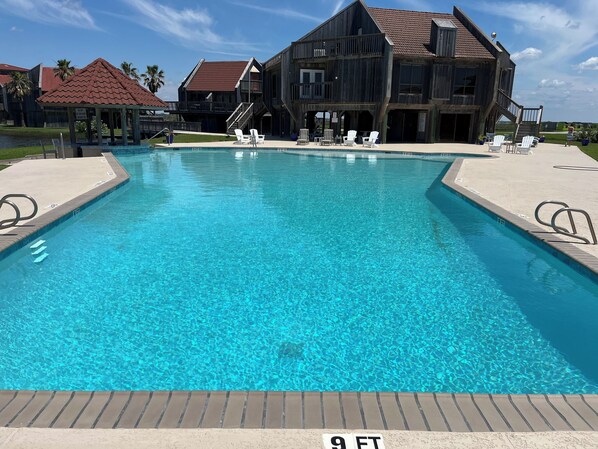 A swimming pool with a 9 ft depth marker, surrounded by lounge chairs and a wooden building with a red roof.