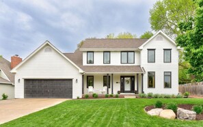A two-story house with a garage, a front porch with chairs, and a well-maintained lawn. - Big Beautiful Abode in Omaha- 4 bedrooms and on a walking trail to Zorinsky Lake (Omaha)