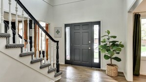 Una escalera con balaustres blancos y barandillas negras, una puerta oscura con un símbolo de cruz, y una planta en maceta.
