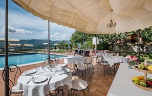 Un espace de restauration en plein air, avec des tables dressées pour le repas, offrant une vue sur une piscine et un paysage montagneux.