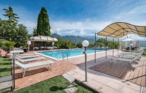 Un espace piscine doté de chaises longues, d’une pergola et offrant une vue sur les montagnes.