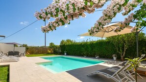 En baghave med swimmingpool, udendørs møbler og en pergola dækket af blomsterklædende vinstokke.