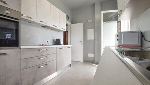 Een moderne keuken met grijze kastjes, roestvrijstalen apparatuur en een betegelde vloer.