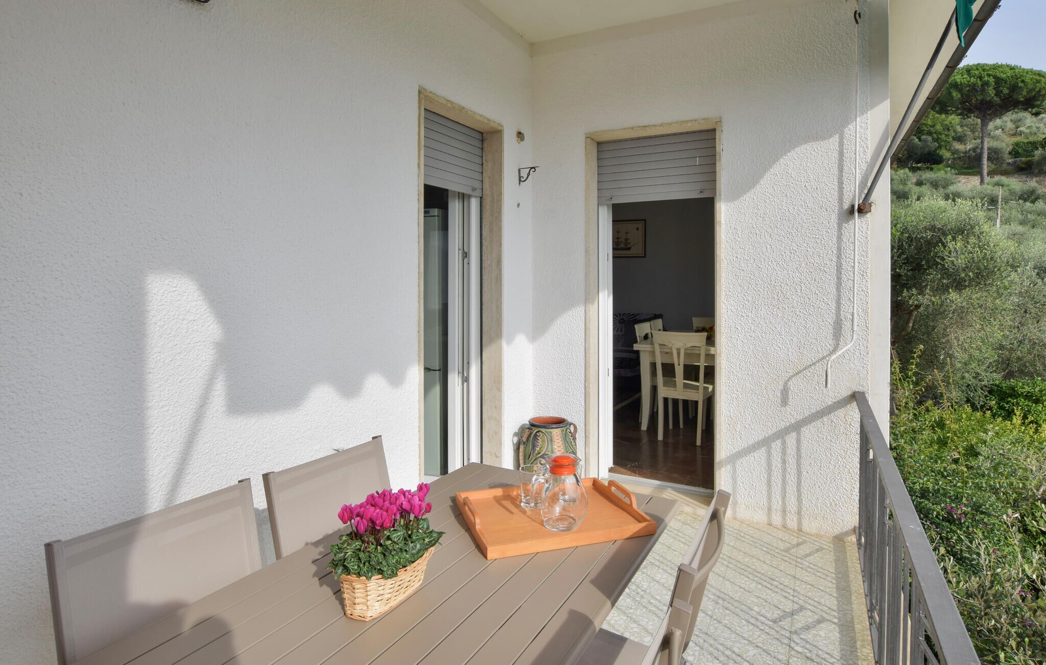Een balkon met een houten tafel, stoelen, een rieten mand met bloemen en een dienblad met een glazen pot en een fles.