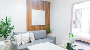 Een moderne woonkamer met een grijze bank, witte kussens, een houten accentmuur, een witte tafel en een pot met een plant.