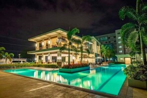 Un hotel con piscina, palmeras y fachada iluminada durante la noche.