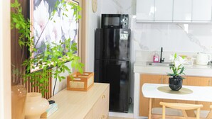 Een moderne keuken met een zwarte koelkast, een houten kast, een wit aanrechtblad en een eethoek met een witte tafel en houten stoelen.