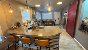 Una cocina moderna con una isla grande, taburetes de bar, luces colgantes y una puerta roja.