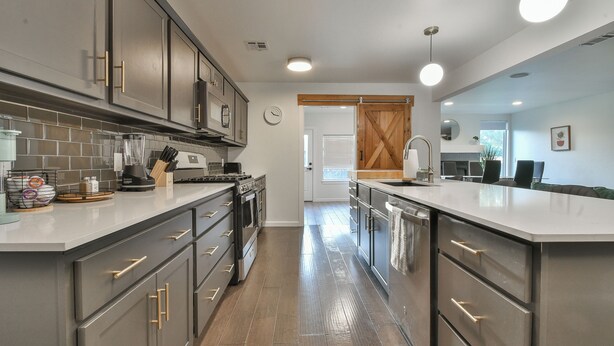 A modern kitchen with grey cabinetry, stainless steel appliances, and a clean, tiled backsplash.
