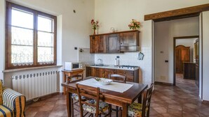 Une cuisine de taille réduite comprenant une table à manger, des placards en bois, une fenêtre et un radiateur.