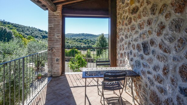Un balcon avec une table et une chaise, donnant sur un paysage pittoresque, avec des arbres et des collines.