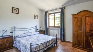 Une chambre à coucher avec un lit, une armoire en bois, une fenêtre avec des rideaux et un radiateur.