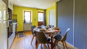 Zona pranzo con tavolo imbandito per quattro, cucina con frigorifero e fornello, e porta scorrevole che dà su un balcone.