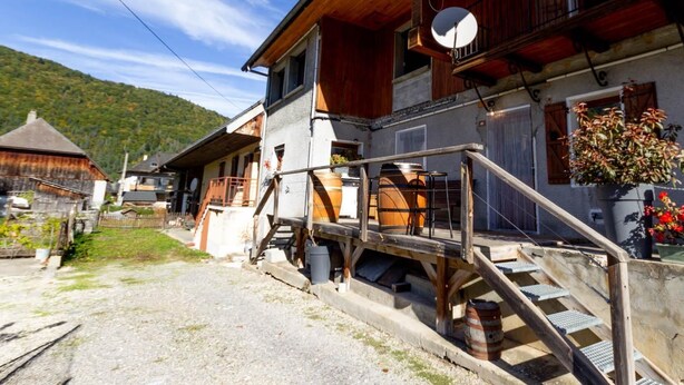 A rustic wooden building with a balcony, a satellite dish, and a small outdoor area with steps leading up to the entrance.