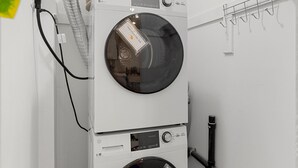 Een gestapelde wasmachine en droger in een wasserij, met een witte muur, een houten vloer en een plafondlamp.