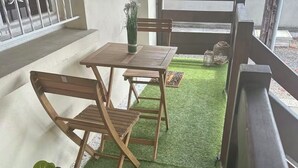 Een balkon met een houten tafel en stoelen, een bloempot en een kleine tuin met kunstgras en decoratieve elementen.